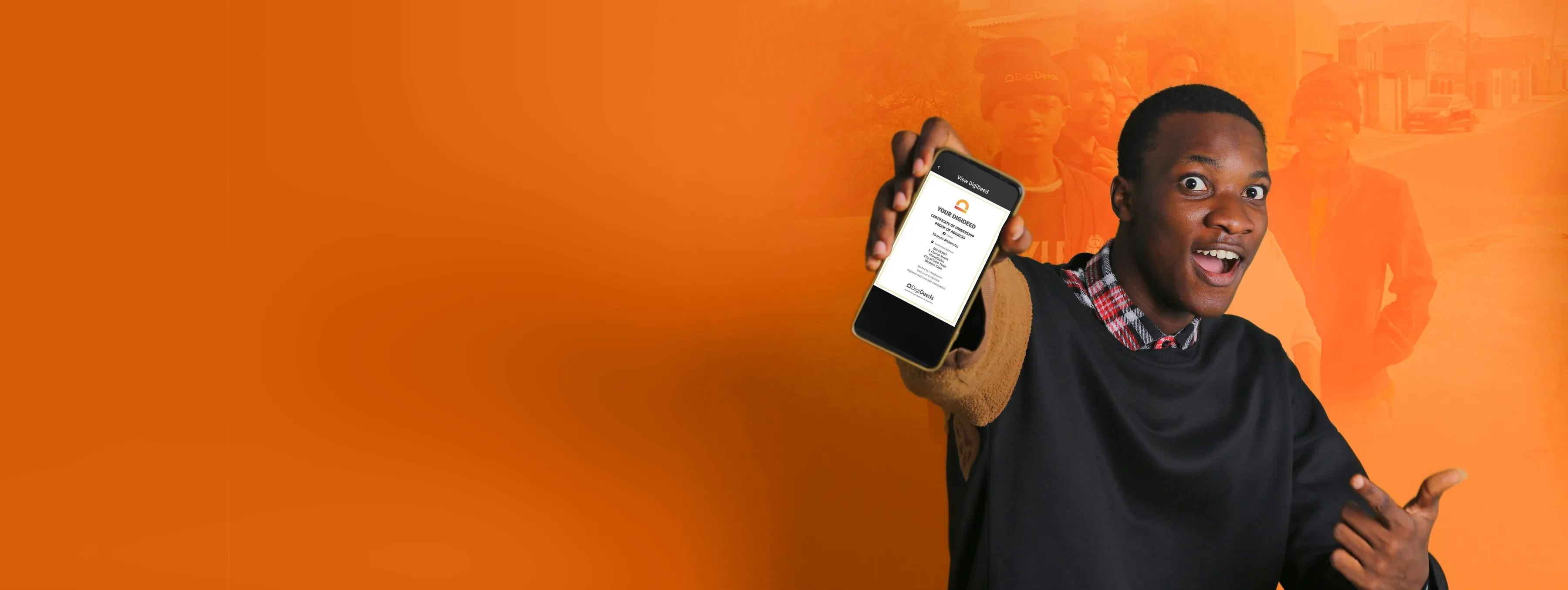 A young man smiles and holds up his phone to show his DigiDeed, with his neighbours standing together behind him