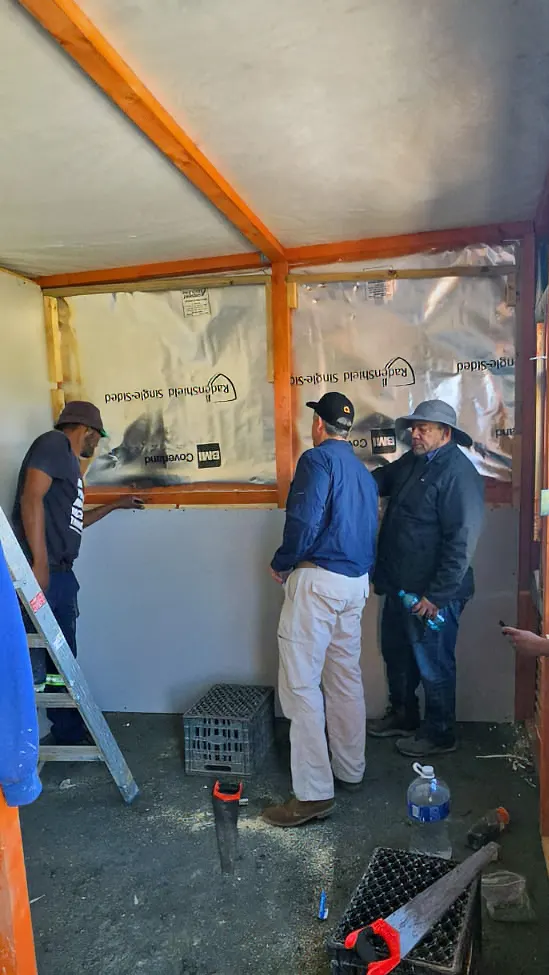 Builders fixing silver insulation inside the timber frame of a new home