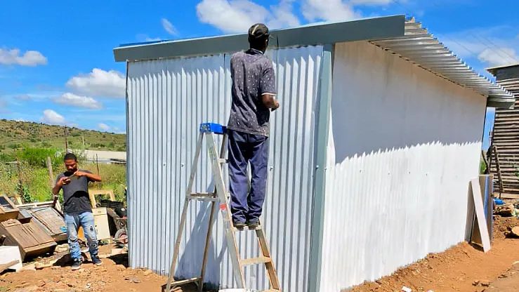 A builder on a ladder finishing the roof edge of a home clad in white corrugated iron
